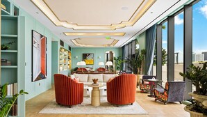 Een ruime lobby met een hoge plafond, een centraal zitgedeelte met twee rode fauteuils, een salontafel en een bank. Grote ramen bieden uitzicht op de stadsgezicht.