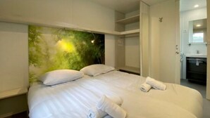 Una habitación de hotel con cama, cabecera con diseño abstracto verde, baño con lavamanos y espejo, y armario.