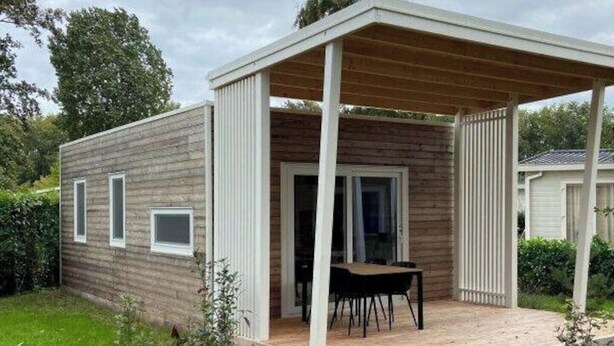 Una casa de una planta con un porche cubierto, un pequeño jardín y una puerta que da al interior.