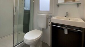Un baño con cabina de ducha de vidrio, inodoro blanco, lavamanos con espejo y repisa de vidrio.