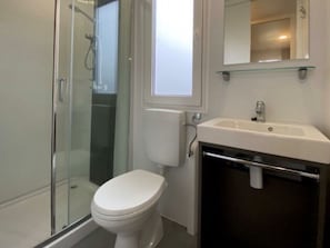 Ein Badezimmer mit Duschkabine aus Glas, einer weißen Toilette, einem Waschbecken mit Spiegel und einer Glasablage.