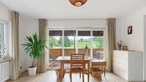 Un comedor con una mesa, sillas, una planta en maceta y vistas a un paisaje verde a través de amplios ventanales.
