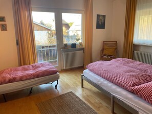 Une chambre avec deux lits, une fenêtre avec des rideaux, un radiateur et une vue sur les bâtiments environnants.