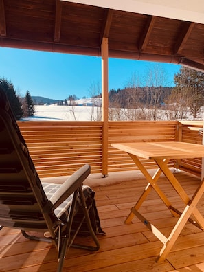Eine Holzterrasse mit Tisch und Stühlen mit Blick auf eine verschneite Landschaft.