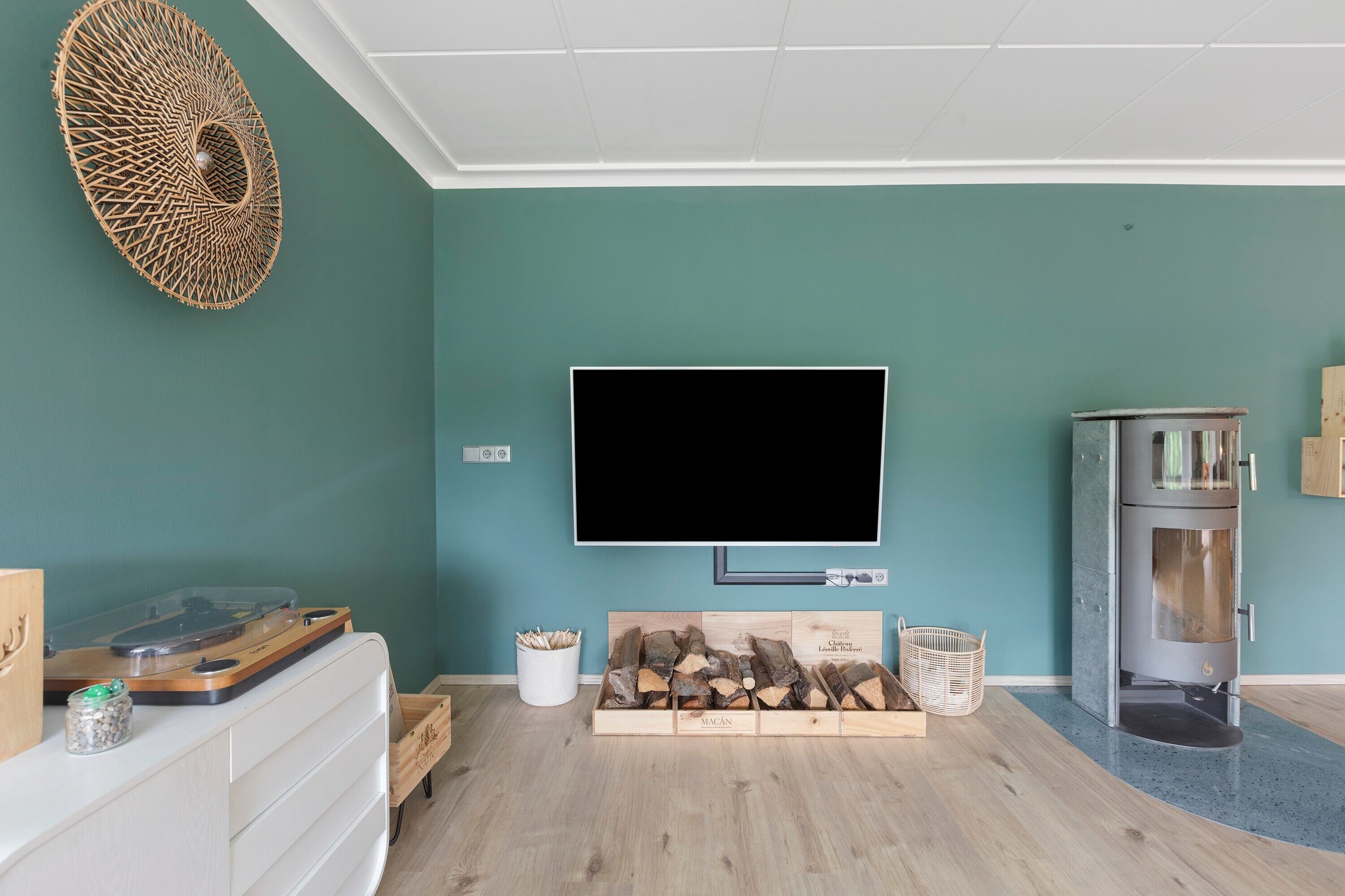 Ein Wohnzimmer mit Flachbildfernseher, Holzscheitvorrat, weißem Schrank und Kamin.
