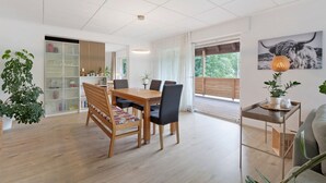 Un comedor moderno con una mesa y sillas de madera, una estantería y un amplio ventanal con vistas a la vegetación.