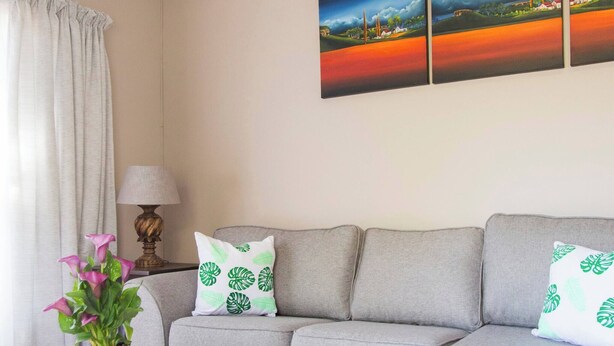 A living room with a grey sofa, a white coffee table, a potted plant, and a wall-mounted painting. - Serene Holiday Retreat Near Hartbeespoort Dam (Hartbeespoort)