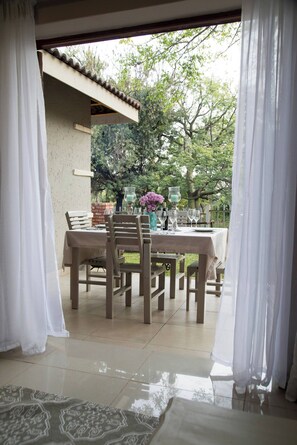 An outdoor dining area with a table set for four, surrounded by chairs, and a view of trees and greenery. - Serene Holiday Retreat Near Hartbeespoort Dam (Hartbeespoort)
