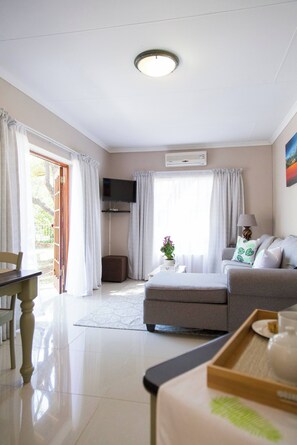 A well-lit living room with a sofa, a television, and a dining area with a table and chairs. - Serene Holiday Retreat Near Hartbeespoort Dam (Hartbeespoort)