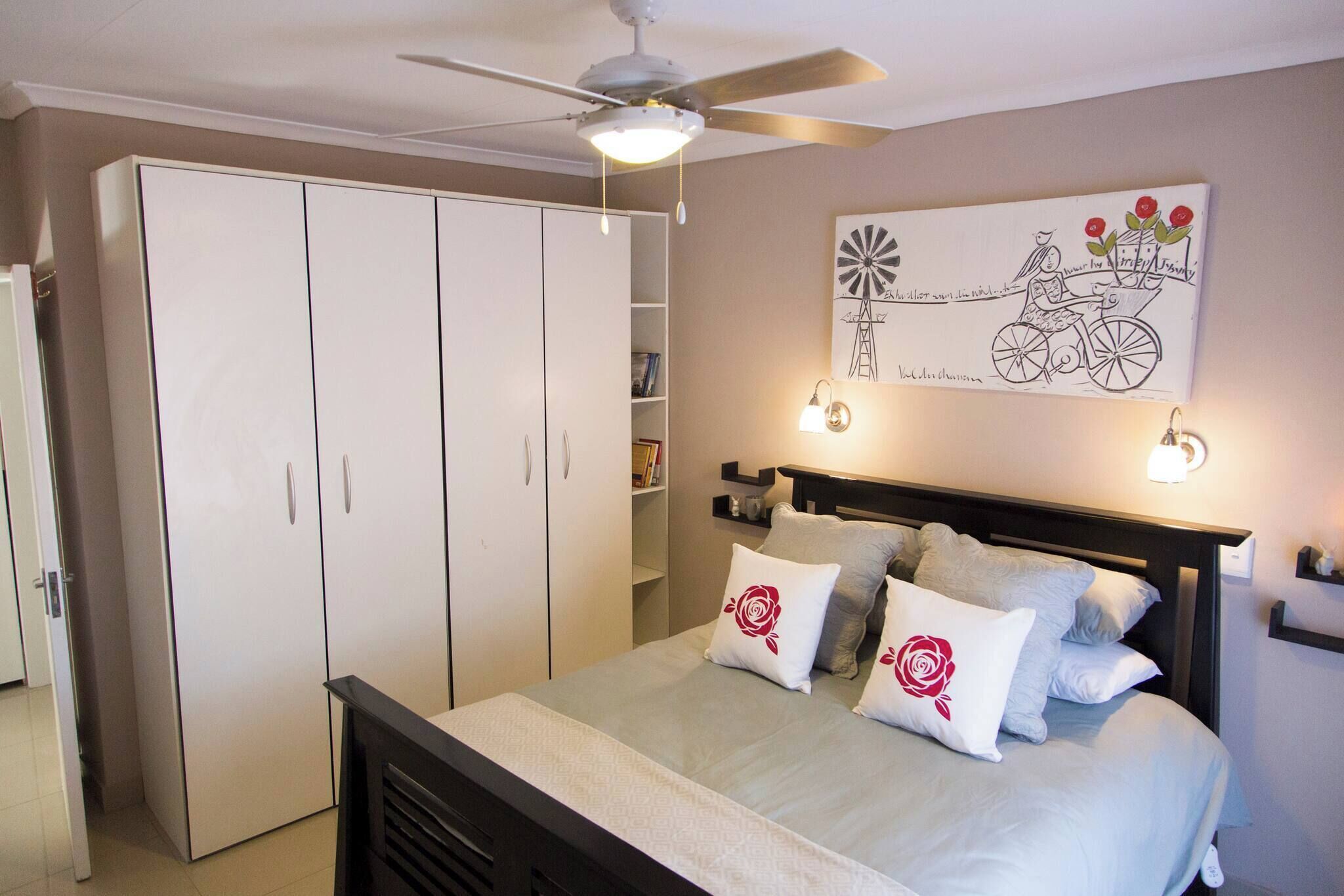 Ein Schlafzimmer mit Bett, Kleiderschrank, Deckenventilator und einem an der Wand hängenden Kunstwerk.