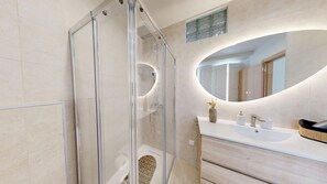 A modern bathroom with a glass-enclosed shower, a round mirror, and a wooden vanity with a sink. - Lobster Room Golfinho (Albufeira)