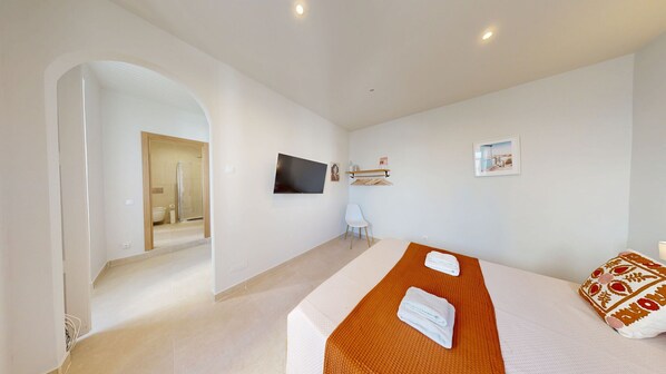 A modern hotel room with a large bed, a television, a shower, and a view of the bathroom.