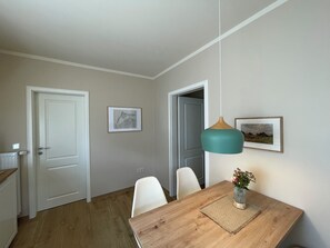 Un comedor con una mesa de madera, sillas blancas, una lámpara colgante y cuadros en la pared.