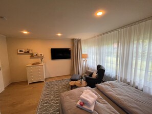 Una habitación de hotel con cama, escritorio, silla, televisor y ventana con cortinas.