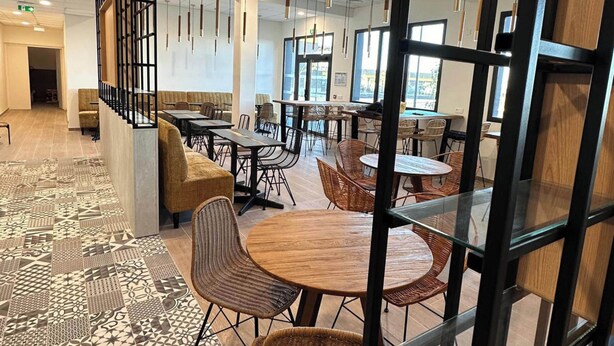 Un restaurante moderno con mesas altas, sillas de mimbre y un piso con diseño.