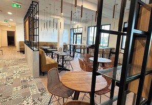 Ein modernes Restaurant mit hohen Tischen, Korbstühlen und einem gemusterten Boden.