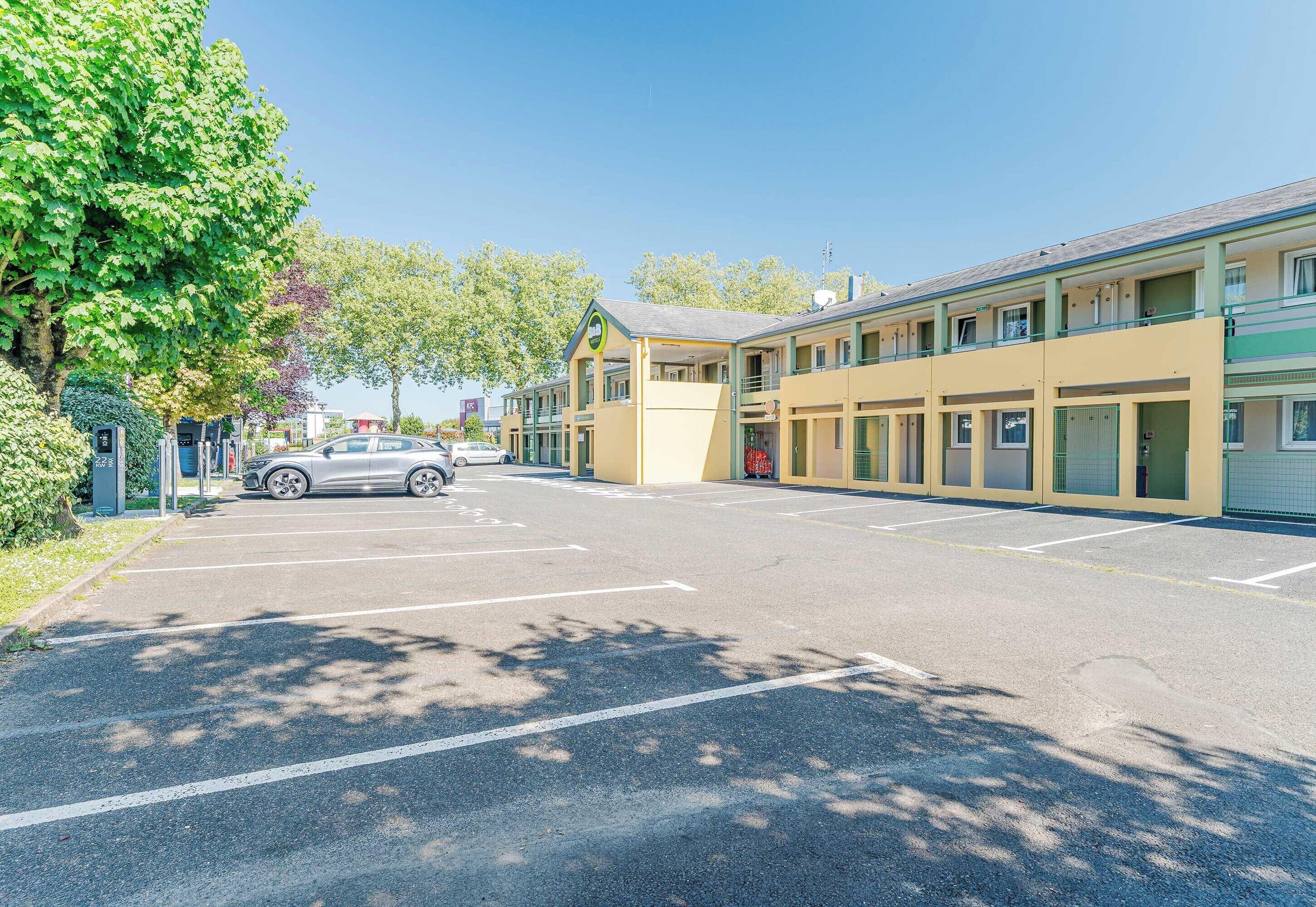 Un motel con estacionamiento, un edificio con toldo verde y una calle arbolada.