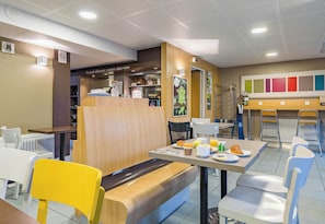 Un espace repas comprenant des tables, des chaises, un banc et un comptoir où sont présentés des aliments.