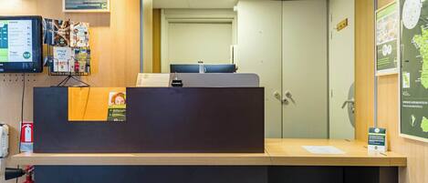 A reception desk with a computer monitor, a fire extinguisher, and informational posters on the wall.