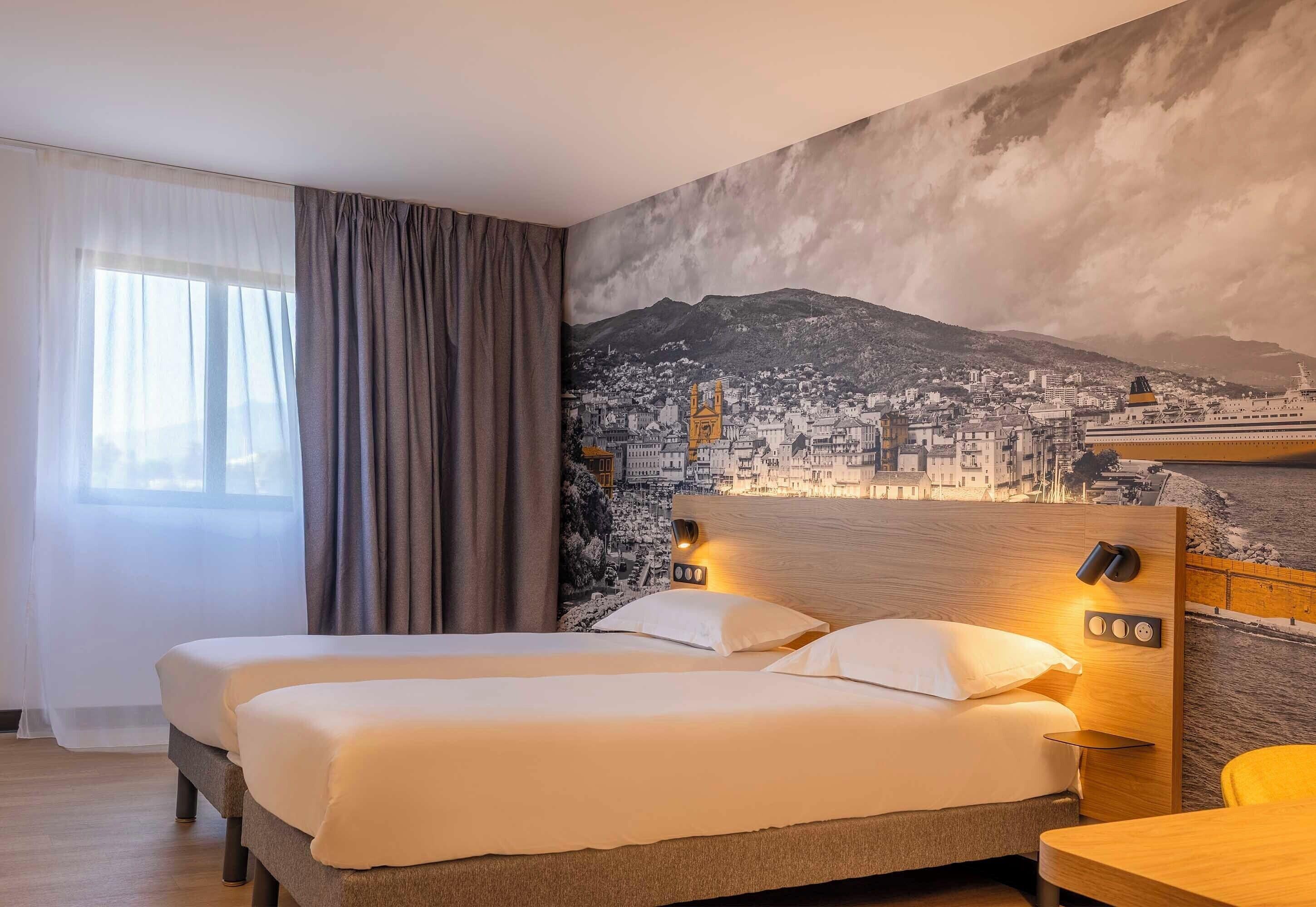 A hotel room with two beds, a cityscape mural, a wooden headboard, and a window with curtains.