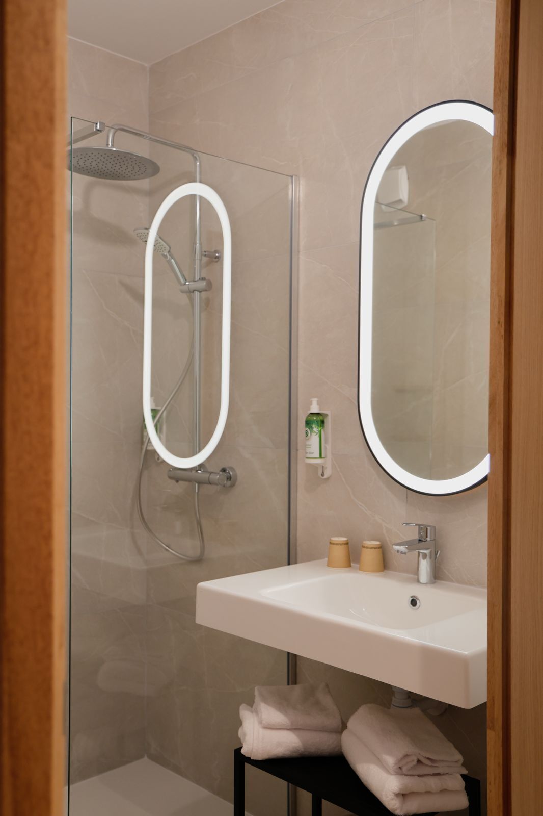 A modern bathroom with a glass-enclosed shower, a white sink with a mirror, and neatly folded towels.
