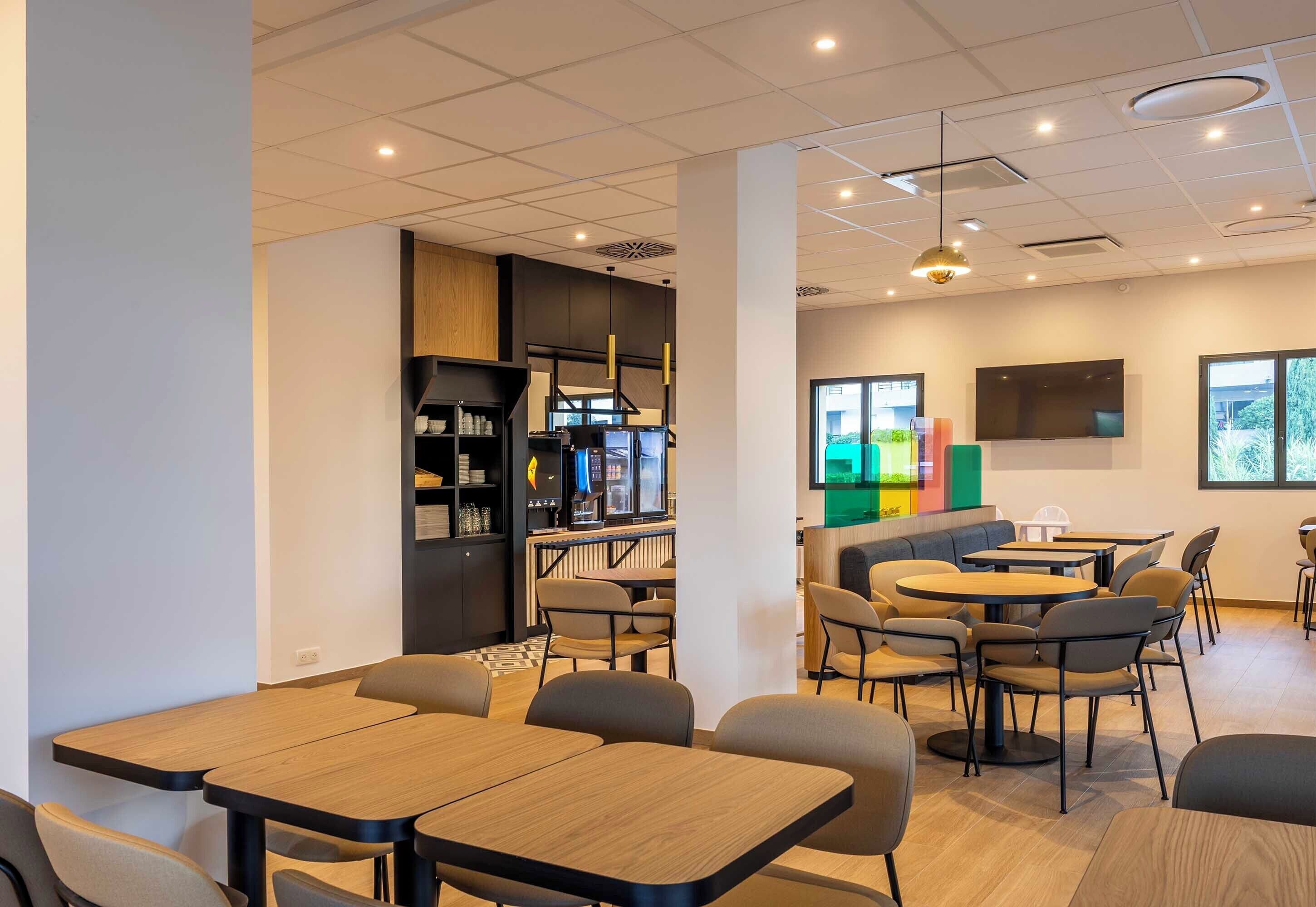 A modern interior with tables and chairs, a counter with a coffee machine, and a TV mounted on the wall.