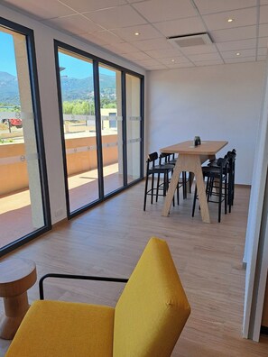 Un interior moderno con ventanas amplias, una mesa de madera con sillas y una butaca amarilla.