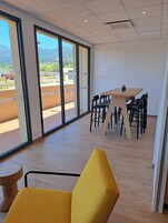 Un interior moderno con ventanas amplias, una mesa de madera con sillas y una butaca amarilla.