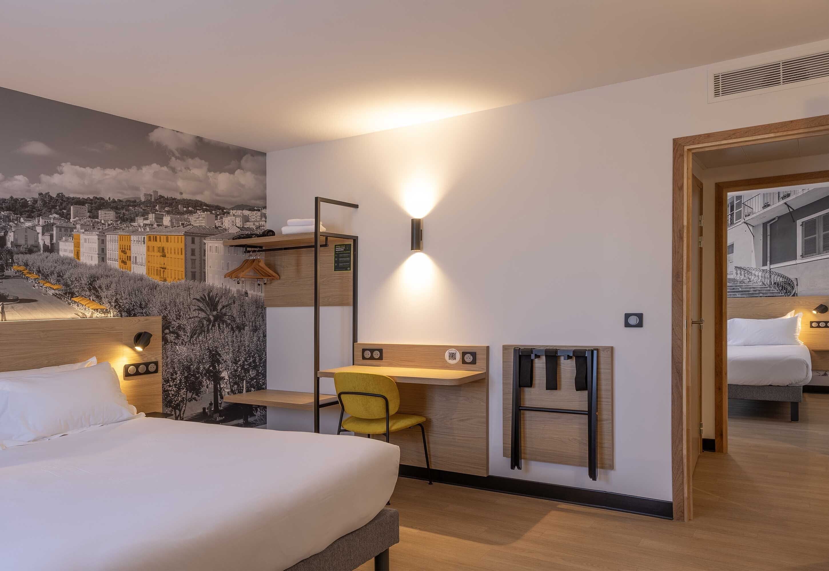 Hotelkamer met een bed, een bureau, een stoel, een kapstok en een muurschildering van een stadsgezicht.