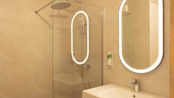 Ein modernes Badezimmer mit einer Glaskabine zur Dusche, einem Waschtisch mit Spiegel und einem wandmontierten Seifenspender.