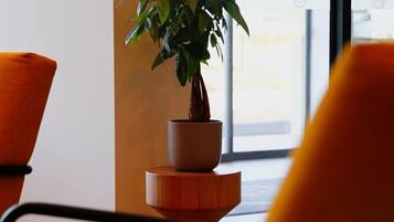 Una planta en maceta sobre un pedestal de madera, una silla y una ventana con vistas.