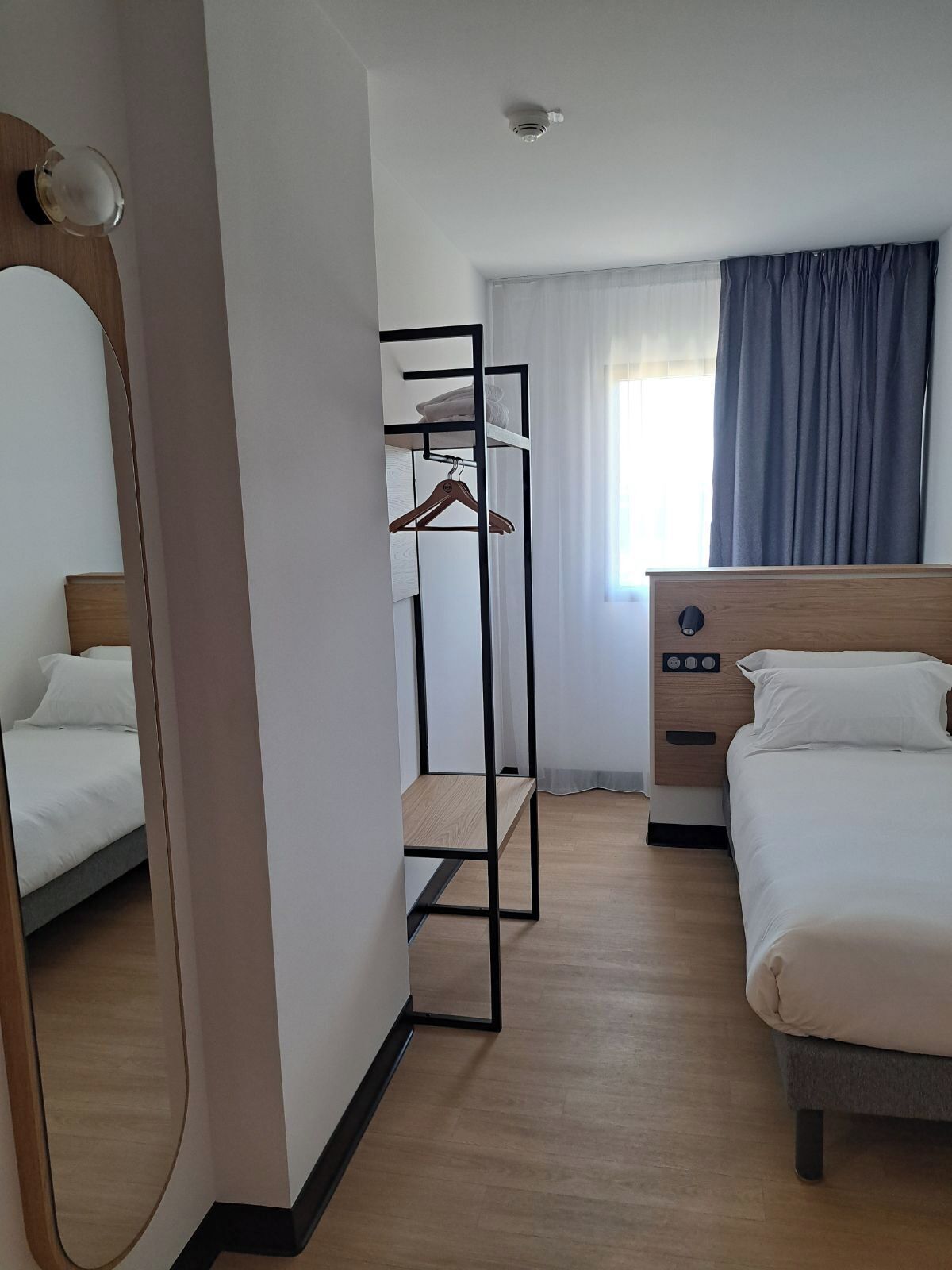A hotel room with a bunk bed, a wooden dresser, a mirror, and a window with curtains.