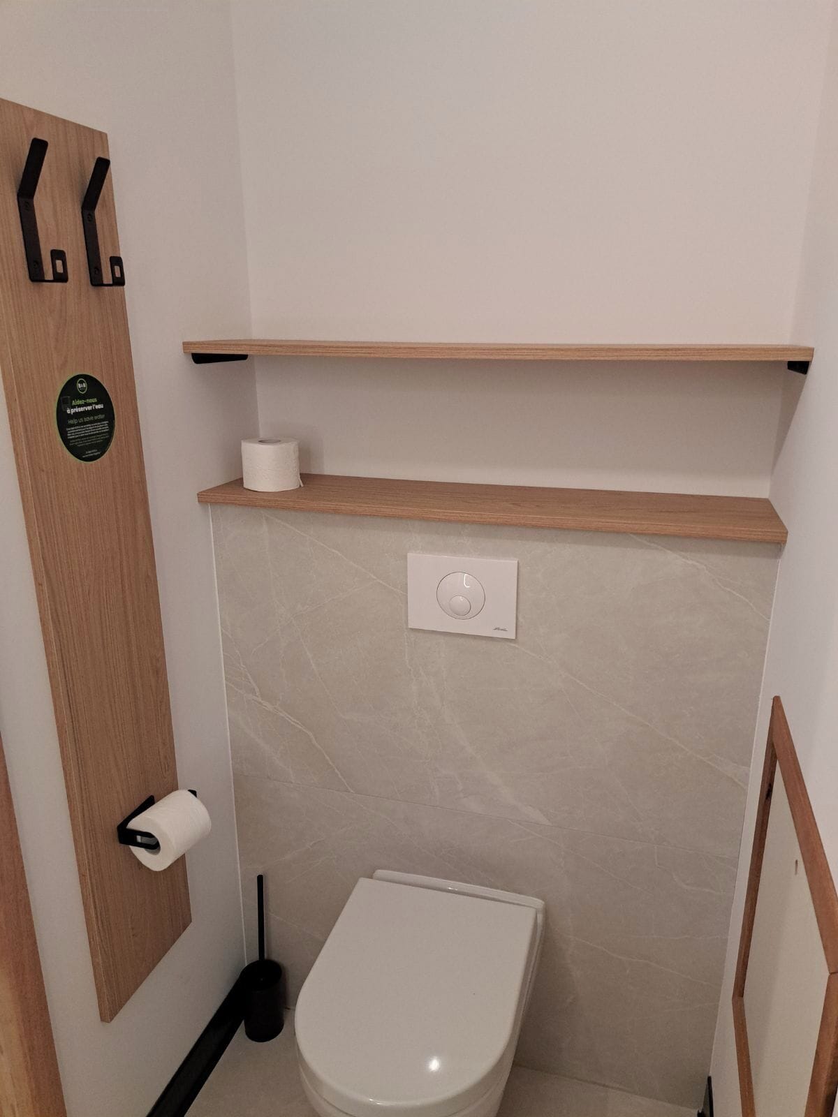 Un baño pequeño con un inodoro, un estante de madera, un dispensador de papel higiénico y un botón de descarga.