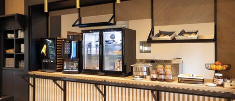 Un espace cuisine moderne équipé d’une machine à café, d’un réfrigérateur et de divers produits alimentaires disposés sur le plan de travail.