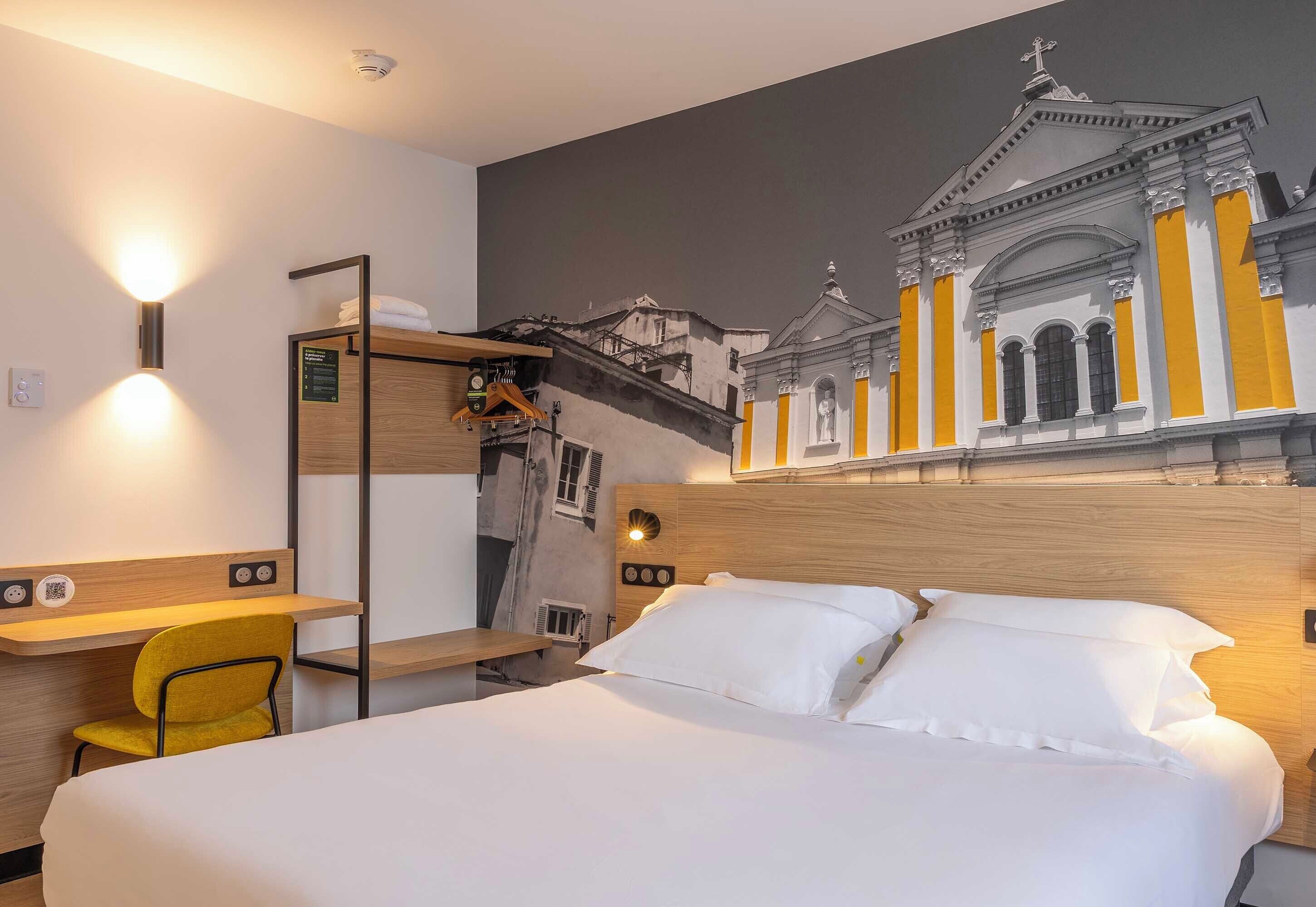 A hotel room with a bed, a desk, a chair, and a wall-mounted shelf.