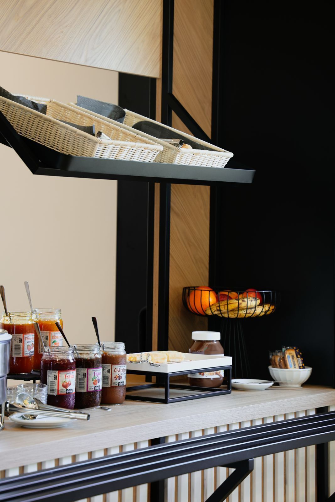 A breakfast bar with wicker baskets, jars of jam, a bowl of fruit, and a bread basket.