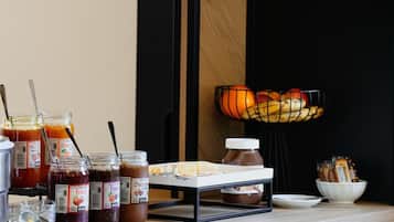 Een ontbijtbuffet met rieten manden, potten jam, een fruitschaal en een broodmand.