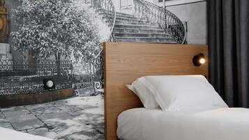 A bedroom with a bed, a headboard, a nightstand, a wall-mounted lamp, and a window with curtains.