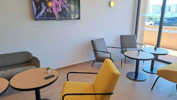 Un intérieur moderne avec un téléviseur fixé au mur, plusieurs options d’assises, notamment un canapé et des fauteuils, ainsi que des tables rondes.