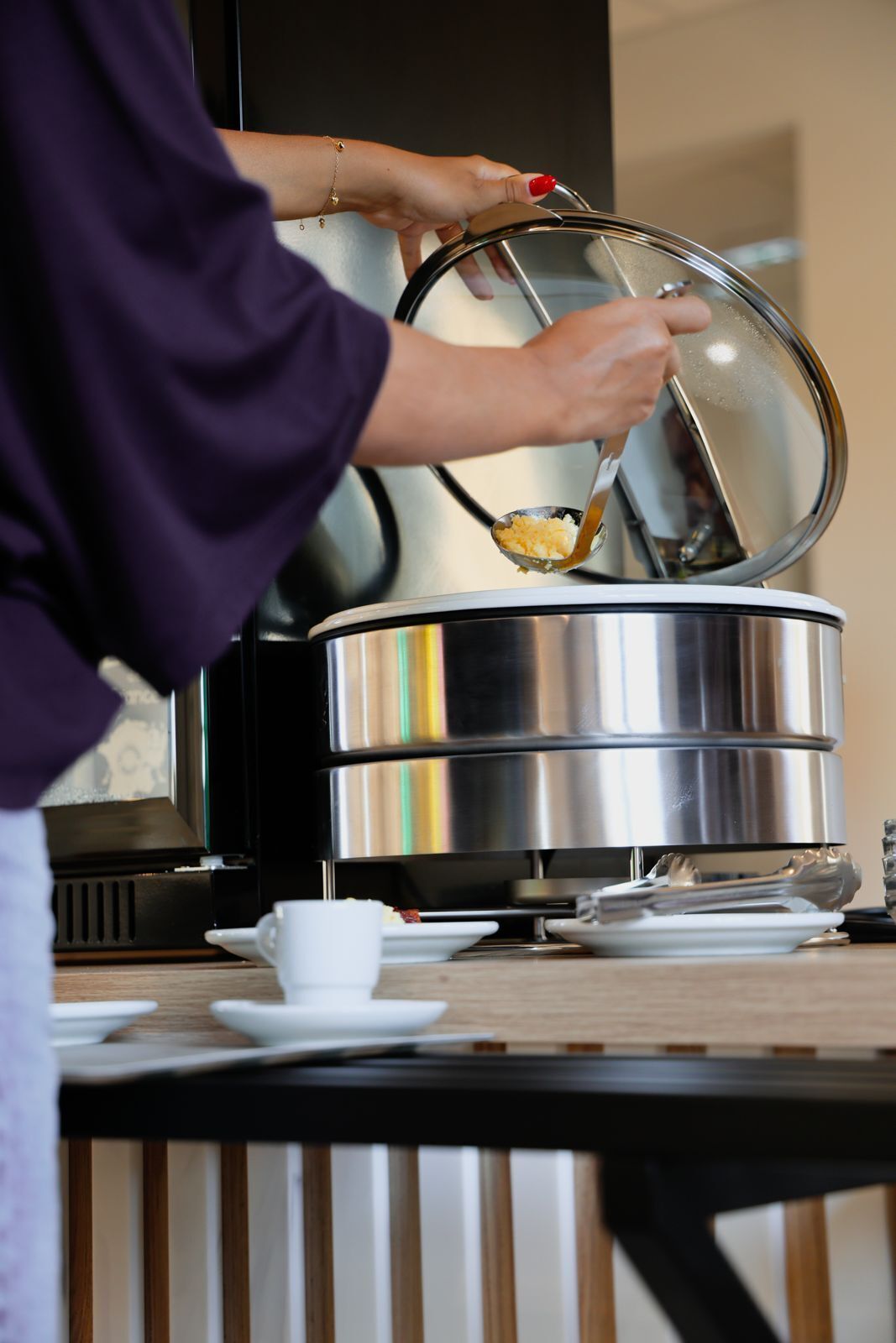 A person serving food from a stainless steel pot on a table with a white cup and saucer.