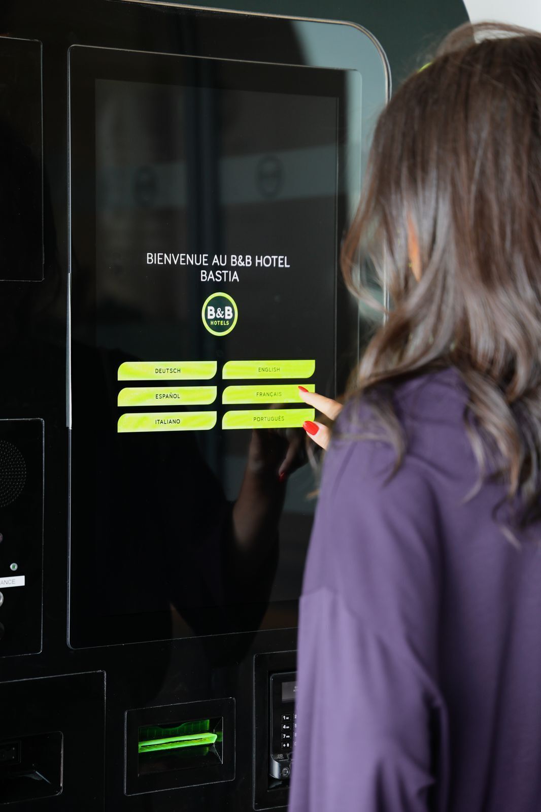 En person använder en digital informationskiosk på B&B Hotel Bastian, där det finns knappar för att välja språk.