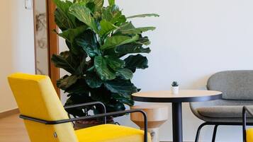 Een gele stoel, een grijze stoel, een ronde tafel en een grote groene plant in een kamer met een houten vloer en een witte muur.