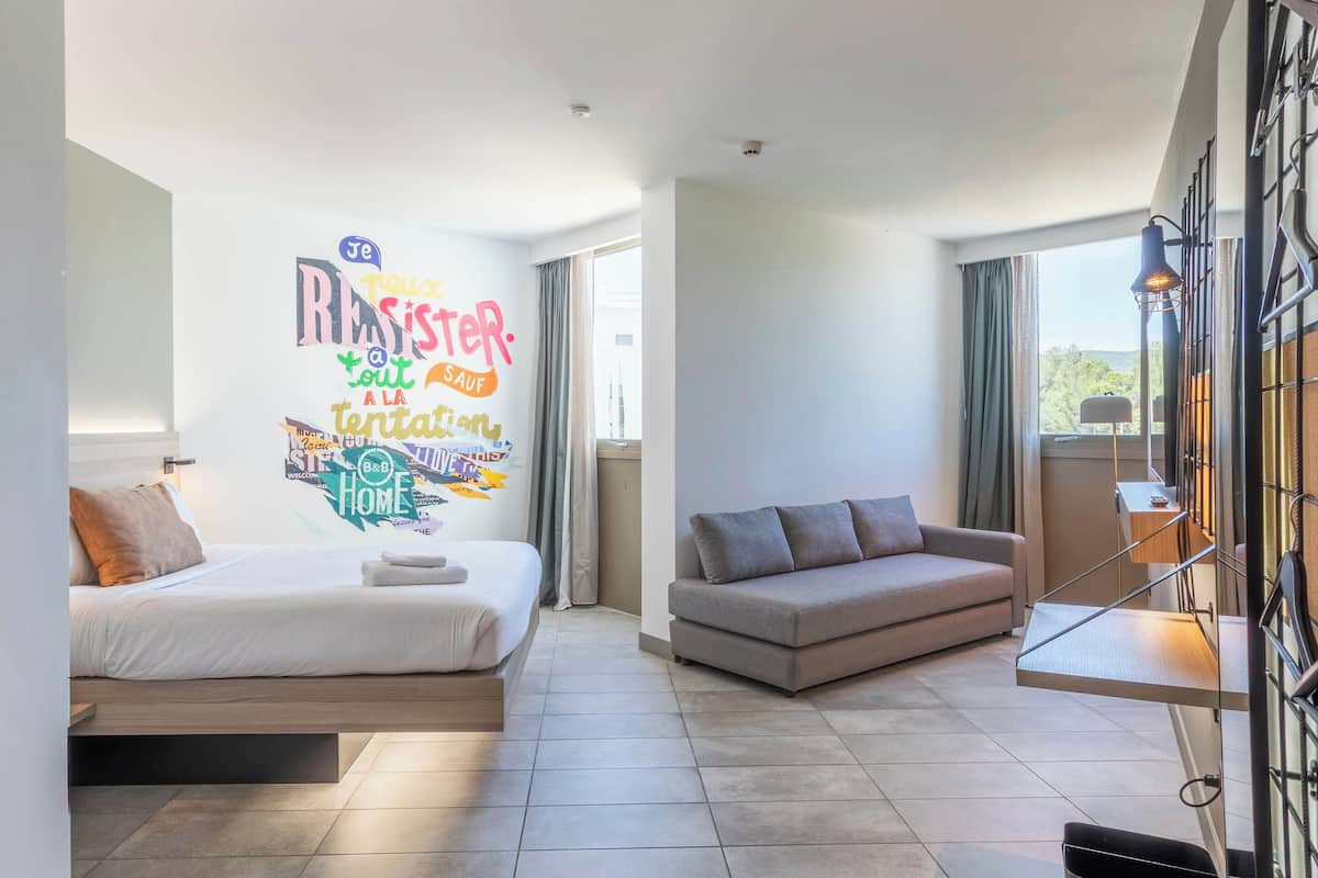 Una habitación de hotel moderna con una cama, un sofá, una obra de arte en la pared y una ventana.