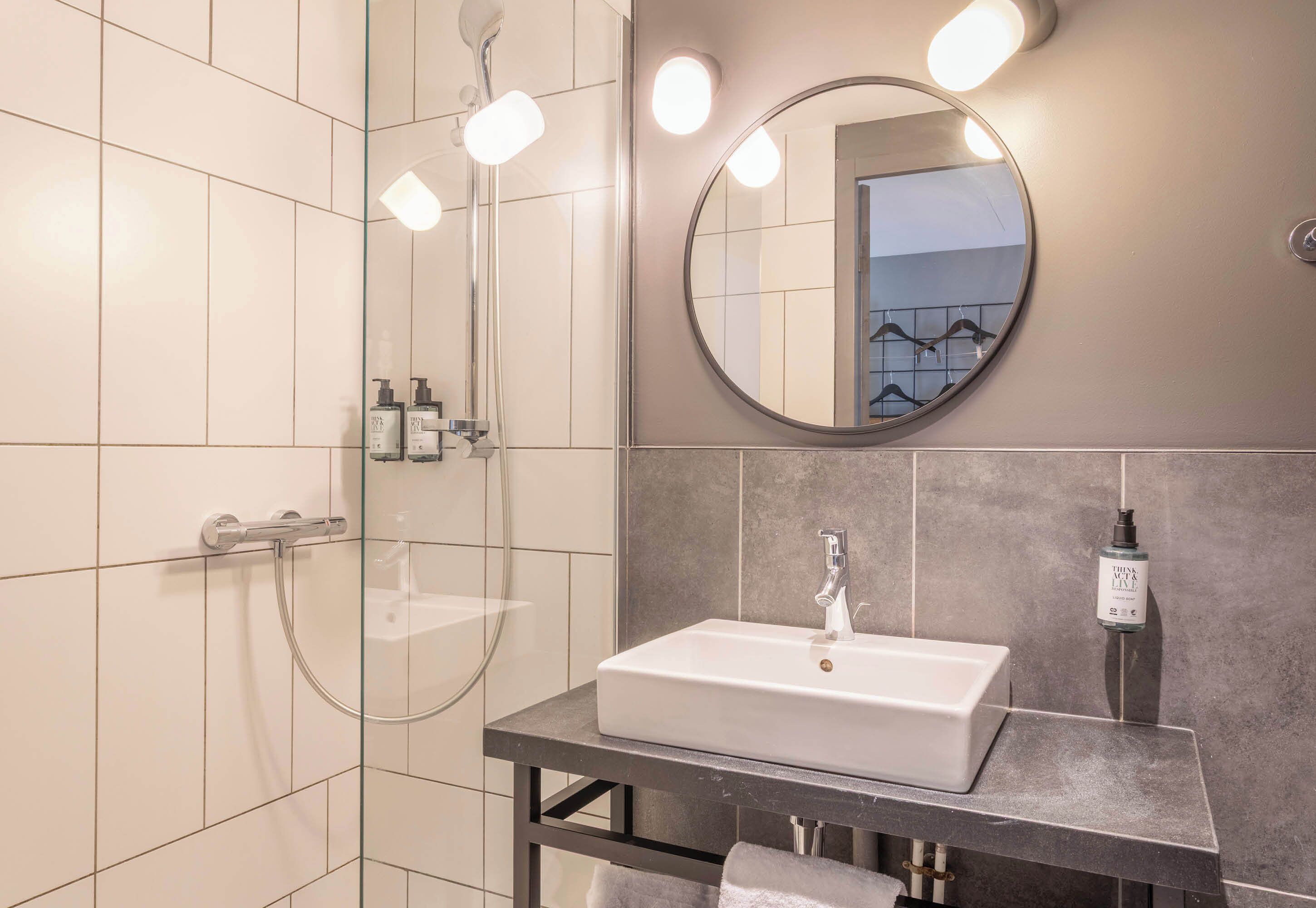 A modern bathroom with a glass shower enclosure, a white sink, and a round mirror.