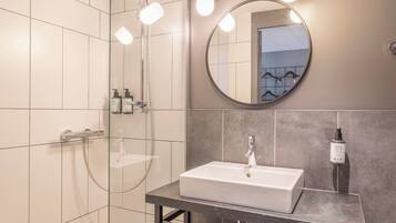 A modern bathroom with a glass shower enclosure, a white sink, and a round mirror.