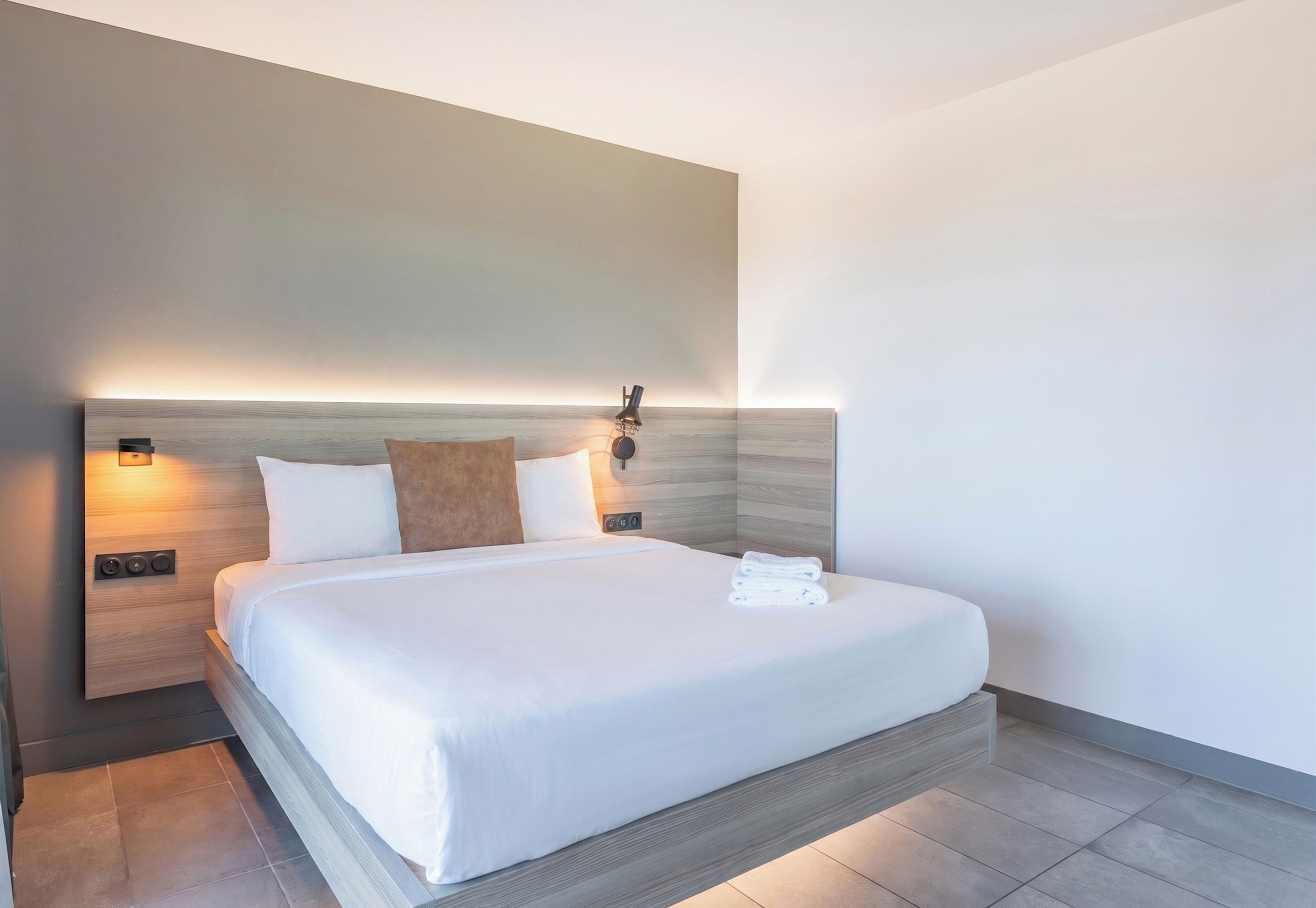 Een moderne hotelkamer met een groot bed, bedlampjes en een wandlamp.
