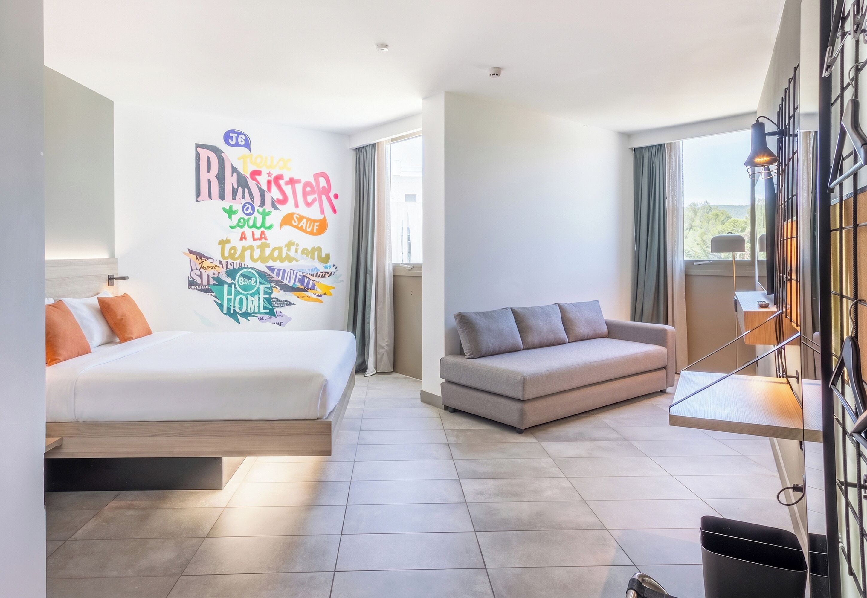 Een moderne hotelkamer met een bed, een bank en een muur met inspirerende stickers.
