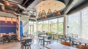 A modern dining area with tables and chairs, large windows, and hanging industrial-style light fixtures.