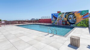 A rooftop pool with a mural, tiled flooring, and a wooden stool.
