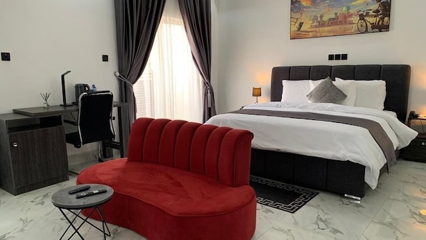 A hotel room with a bed, a red sofa, a desk with a lamp, and a painting on the wall. - Devon's 5BR Villa with Pool, Gym & Bar, gated in Katampe Abuja (Abuja)